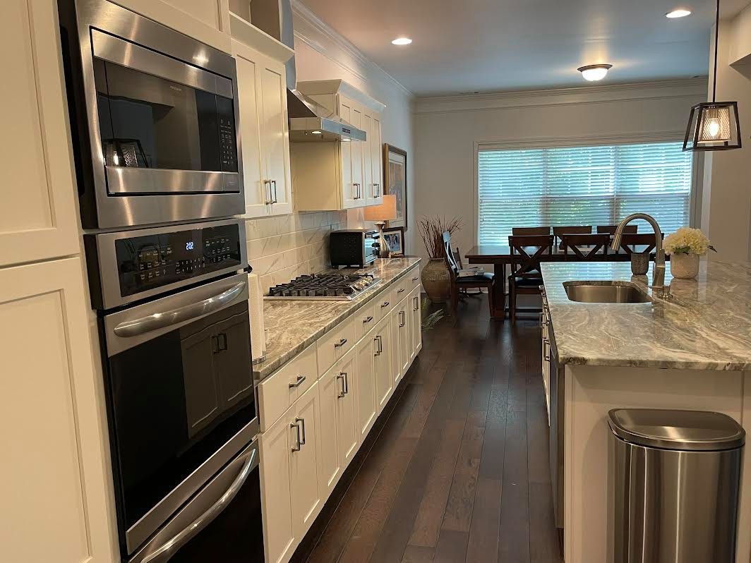 Modern kitchen with white cabinets, stainless steel appliances, granite island, and dark wood floors leading to a dining area