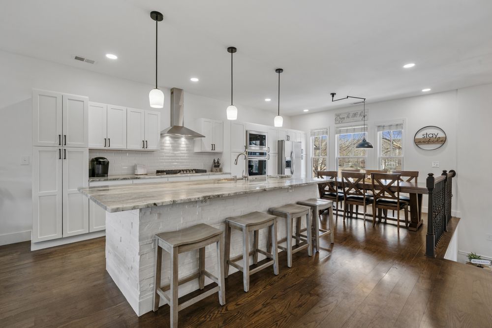 Bright modern kitchen with white cabinets, marble island, and adjacent dining area with hardwood floors