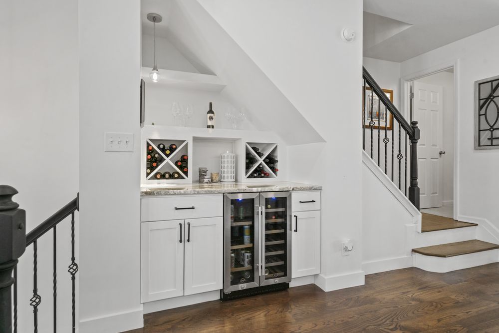 Built-in white bar cabinet with wine fridge and staircase in a bright foyer