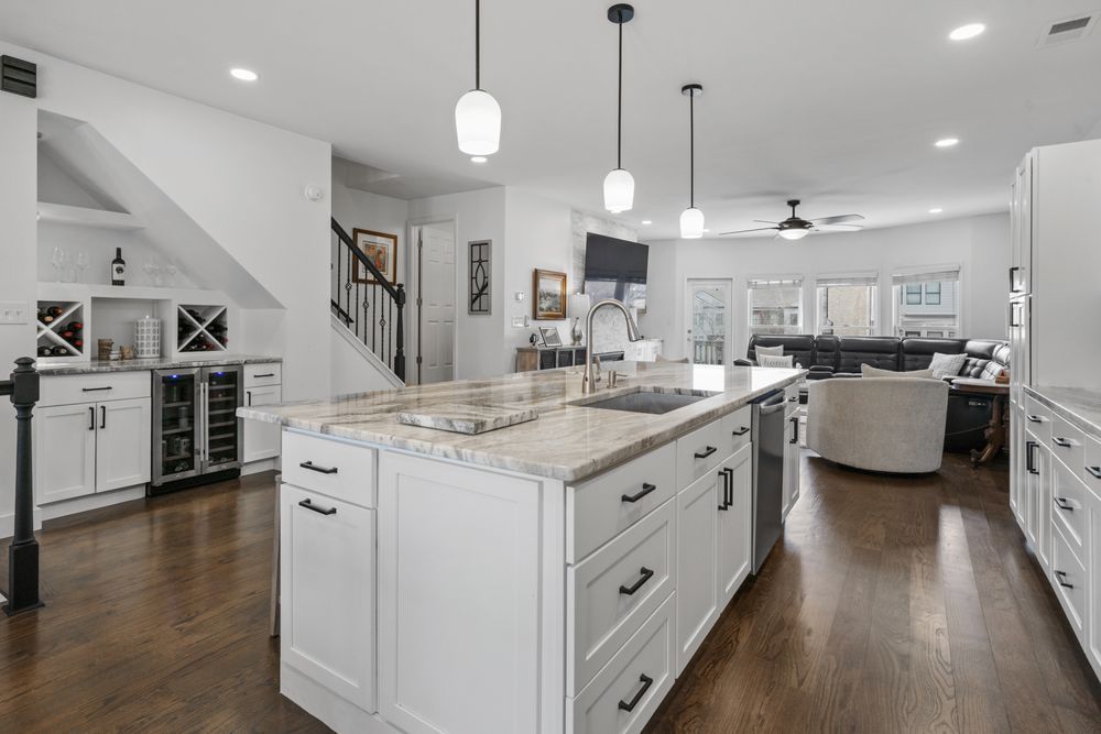 Bright modern kitchen with white cabinets, marble island, pendant lights, and dark wood floors