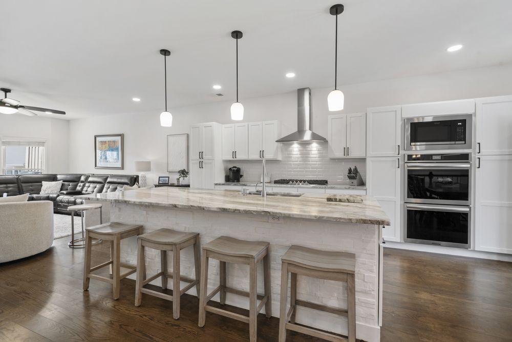 Bright modern kitchen with white island, pendant lights, stools, and double wall ovens