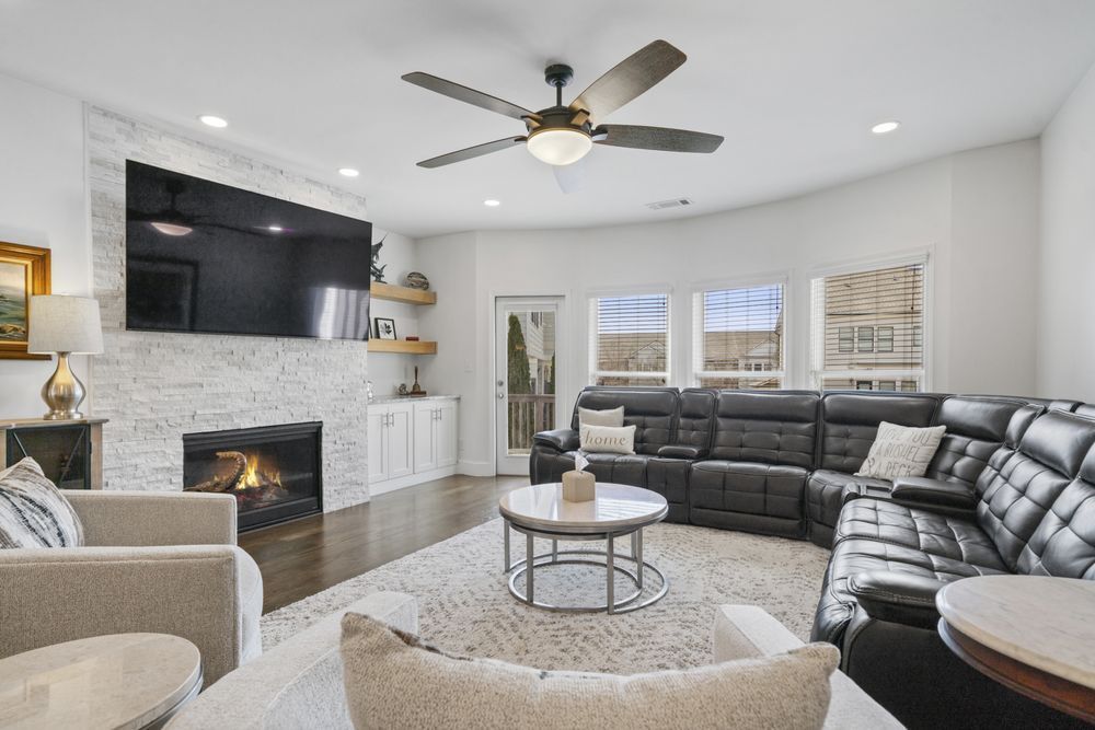 Bright modern living room with black sectional sofa, fireplace, ceiling fan, and light gray decor