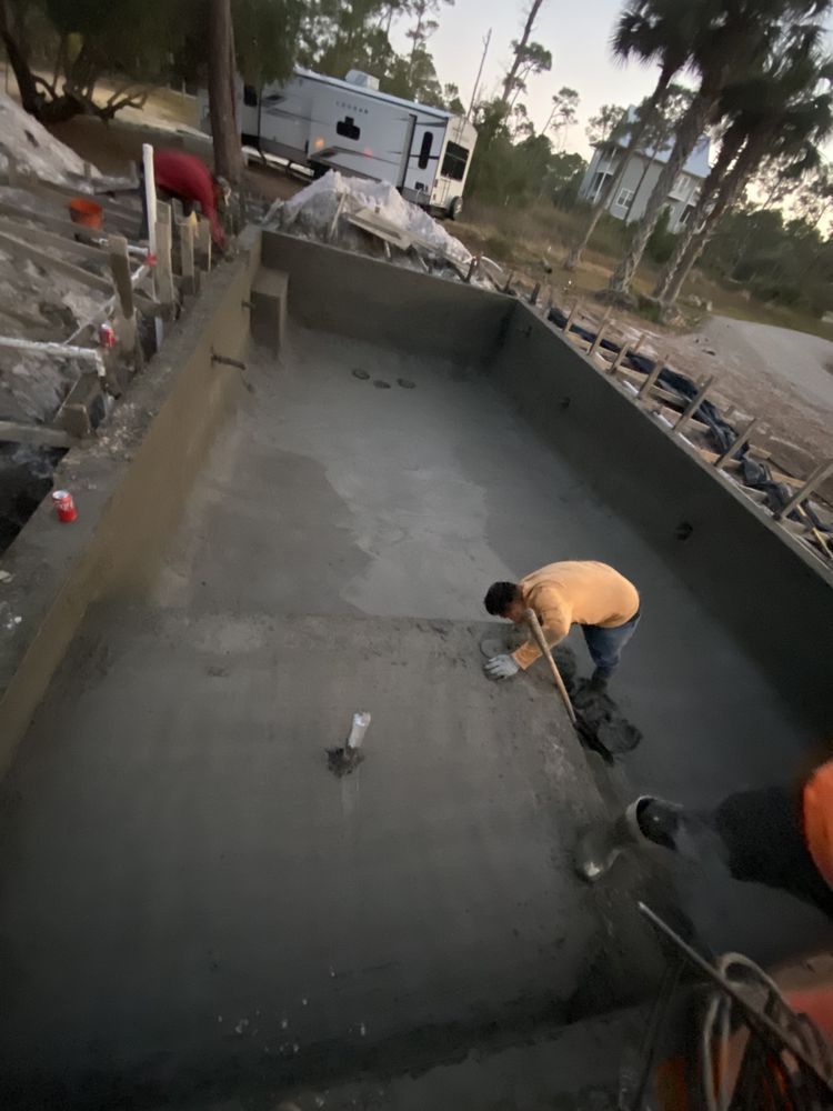 Workers troweling wet concrete inside a large rectangular pool under construction