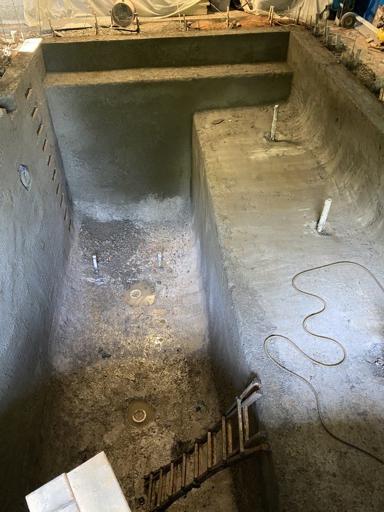 Empty concrete pool under construction with a ladder and hose inside