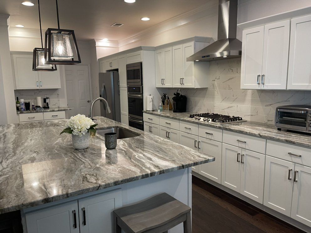 Modern white kitchen with marble island, black pendant lights, and stainless steel appliances