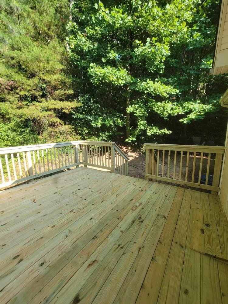 Wooden deck with white railing overlooking a leafy green backyard in sunlight
