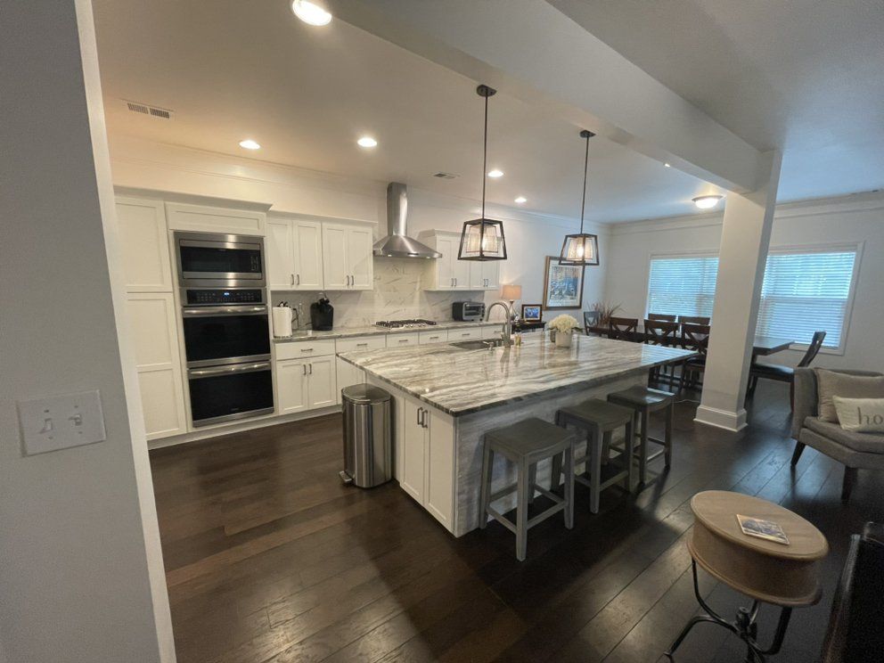 Modern kitchen with white cabinets, marble island, pendant lights, and dark wood floors
