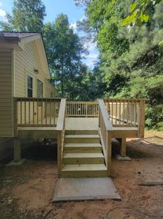 Wooden deck with central stairs leading from a house to a wooded yard, with a concrete landing below