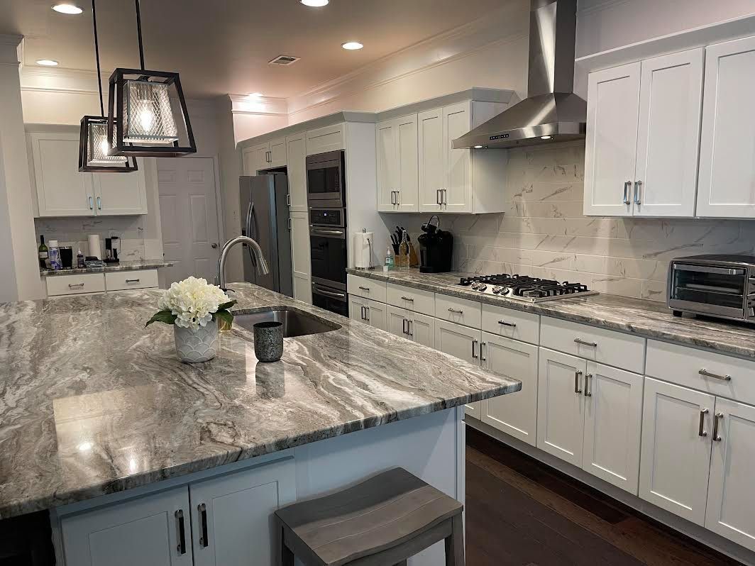 Modern white kitchen with granite island, stainless appliances, pendant lights, and built-in oven and stove.