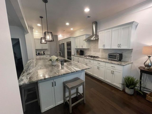 Bright modern kitchen with white cabinets, granite island, pendant lights, and dark wood floors