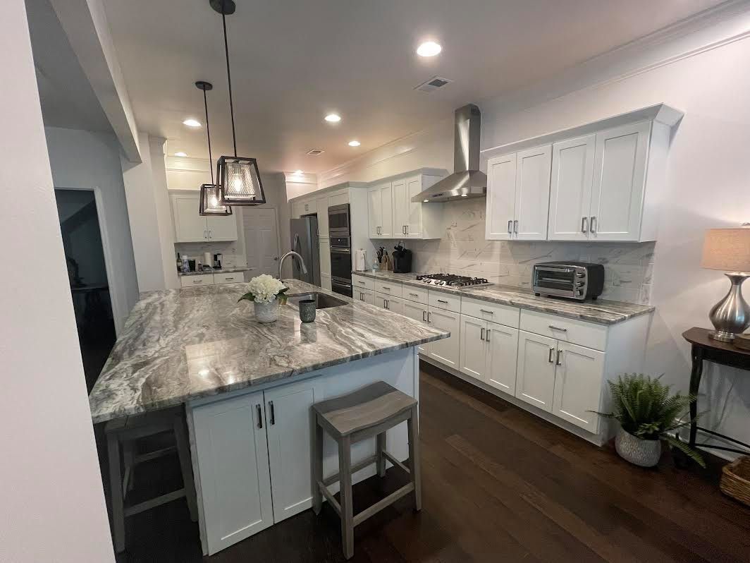 Modern kitchen with white cabinets, granite island, pendant lights, and dark wood flooring