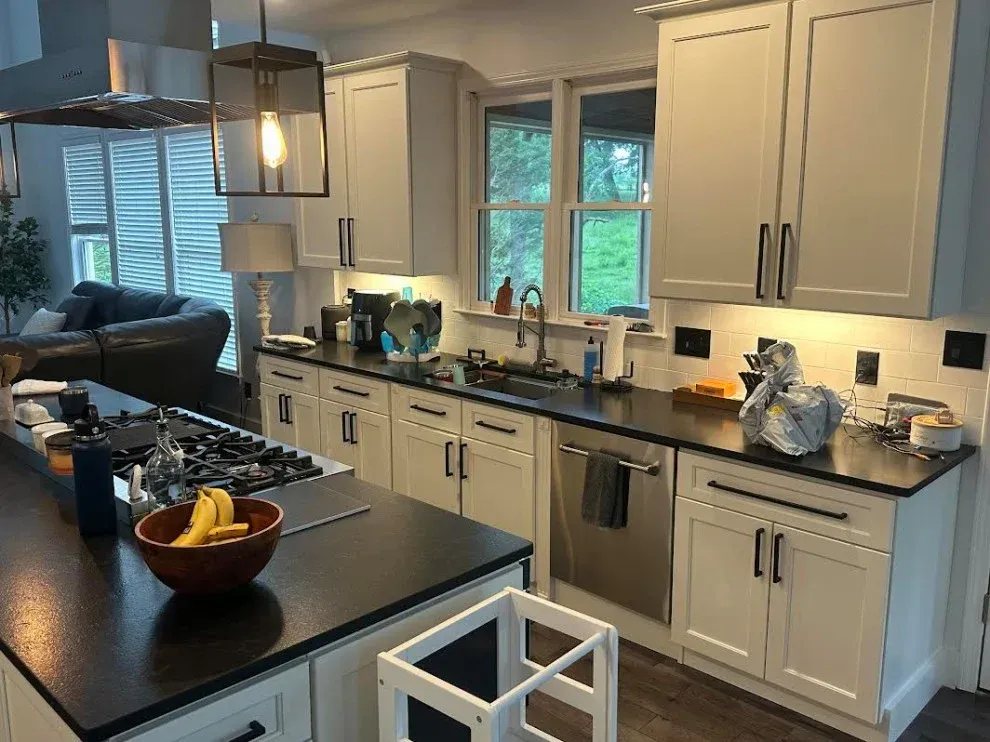 Bright modern kitchen with white cabinets, black countertops, island, and large windows.