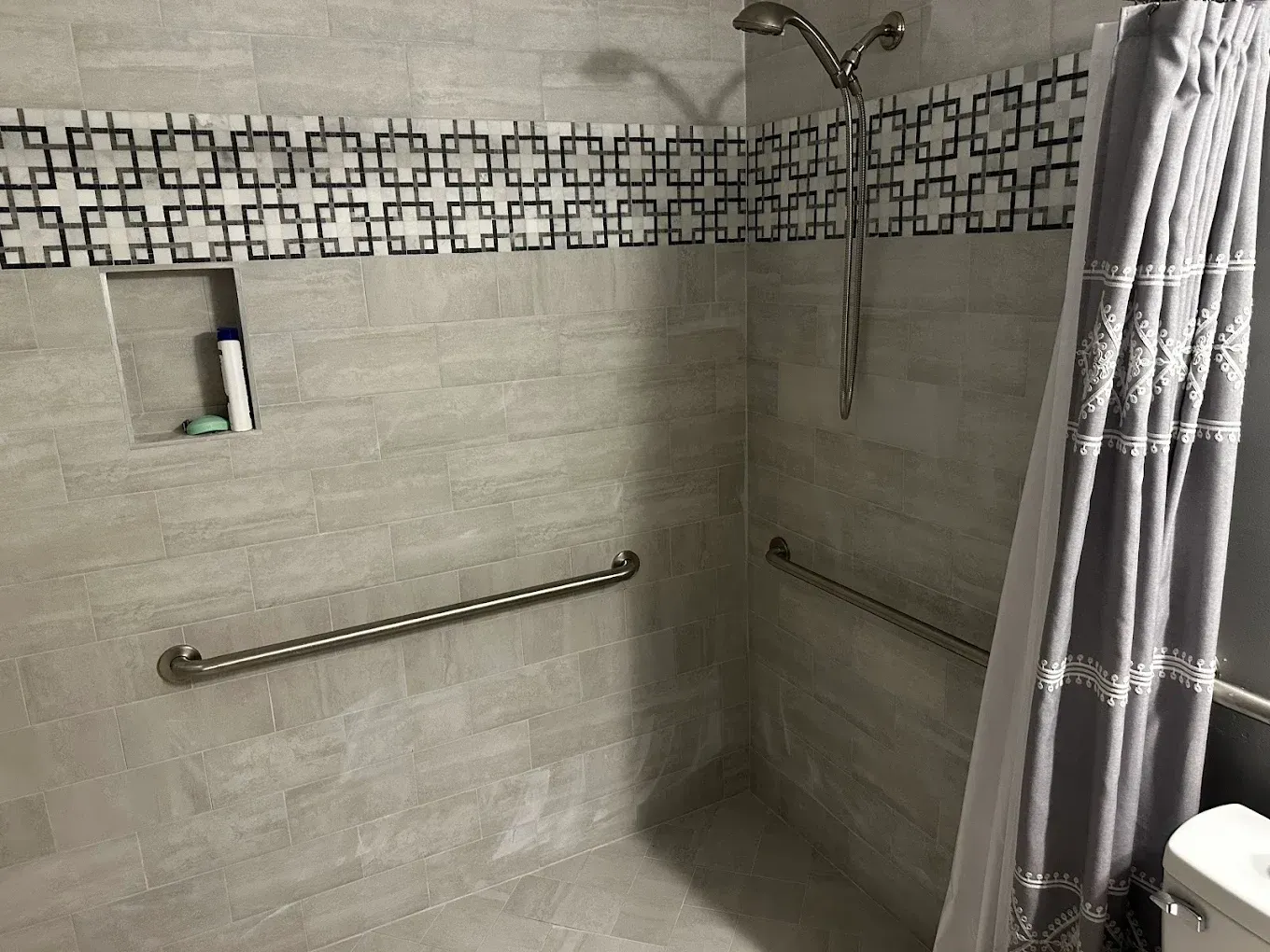 Tiled bathroom shower with grab bars, recessed shelf, and gray curtain