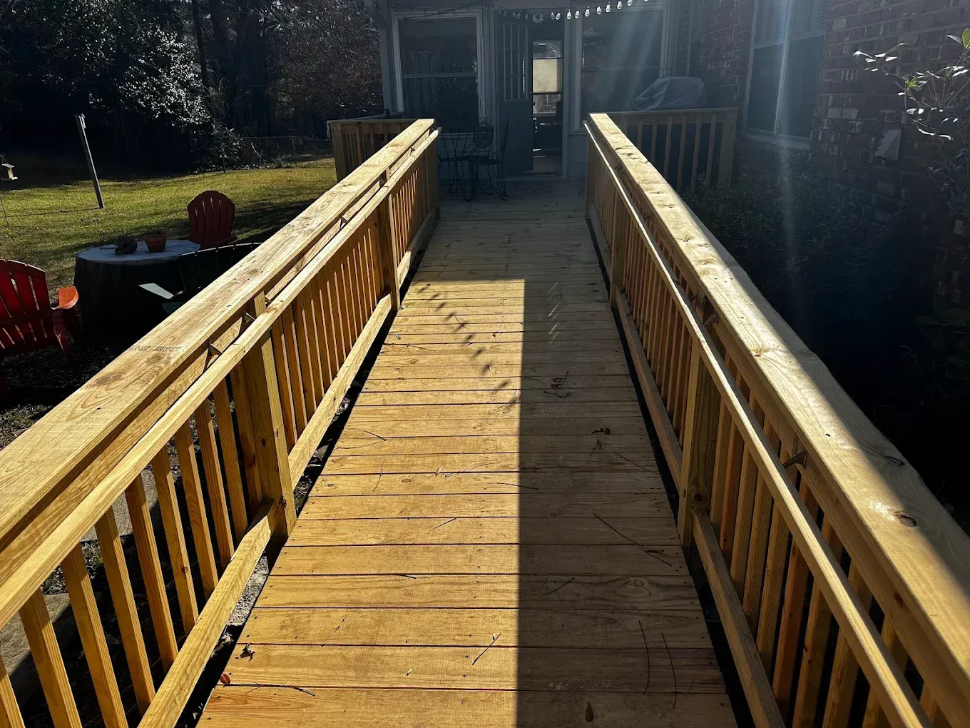 Wooden ramp with railings leading to a building entrance in bright sunlight