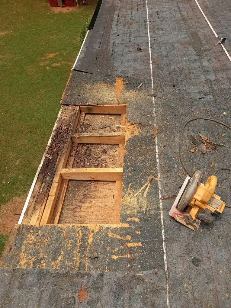 Roof with a large cutout exposing wooden framing, next to a circular saw on the shingles.