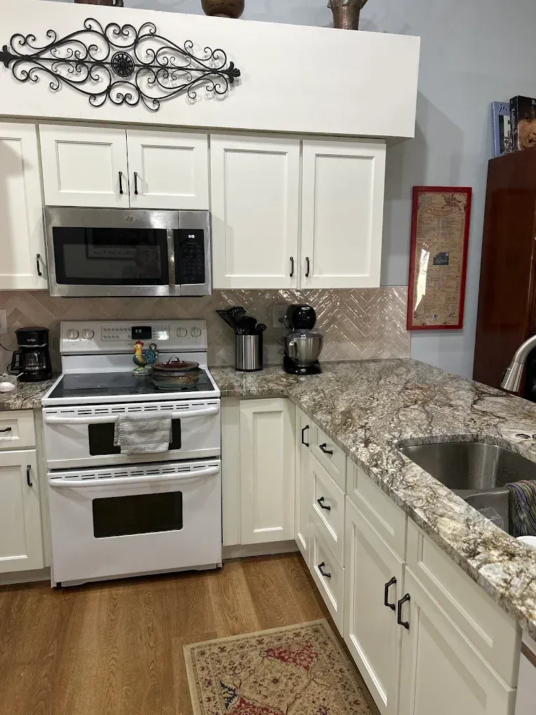 White kitchen with stainless steel stove, microwave, and granite counters beside a double sink.