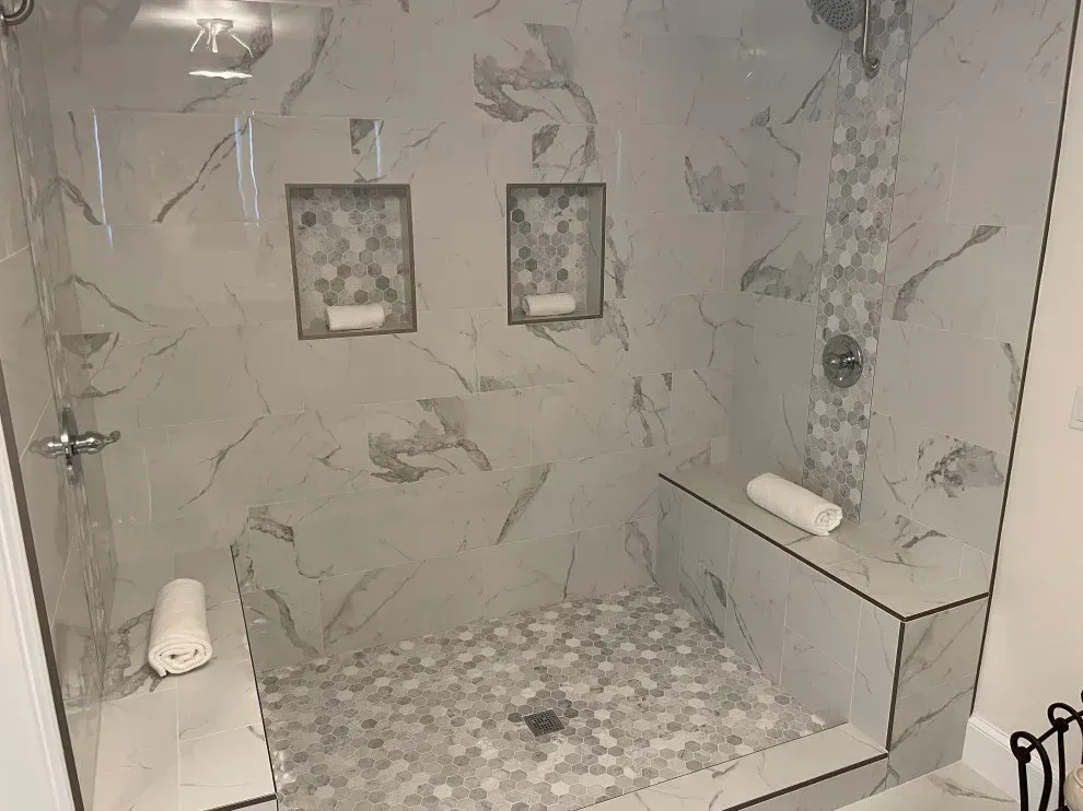 Modern tiled shower with pebble floor, bench, wall niches, and glass door
