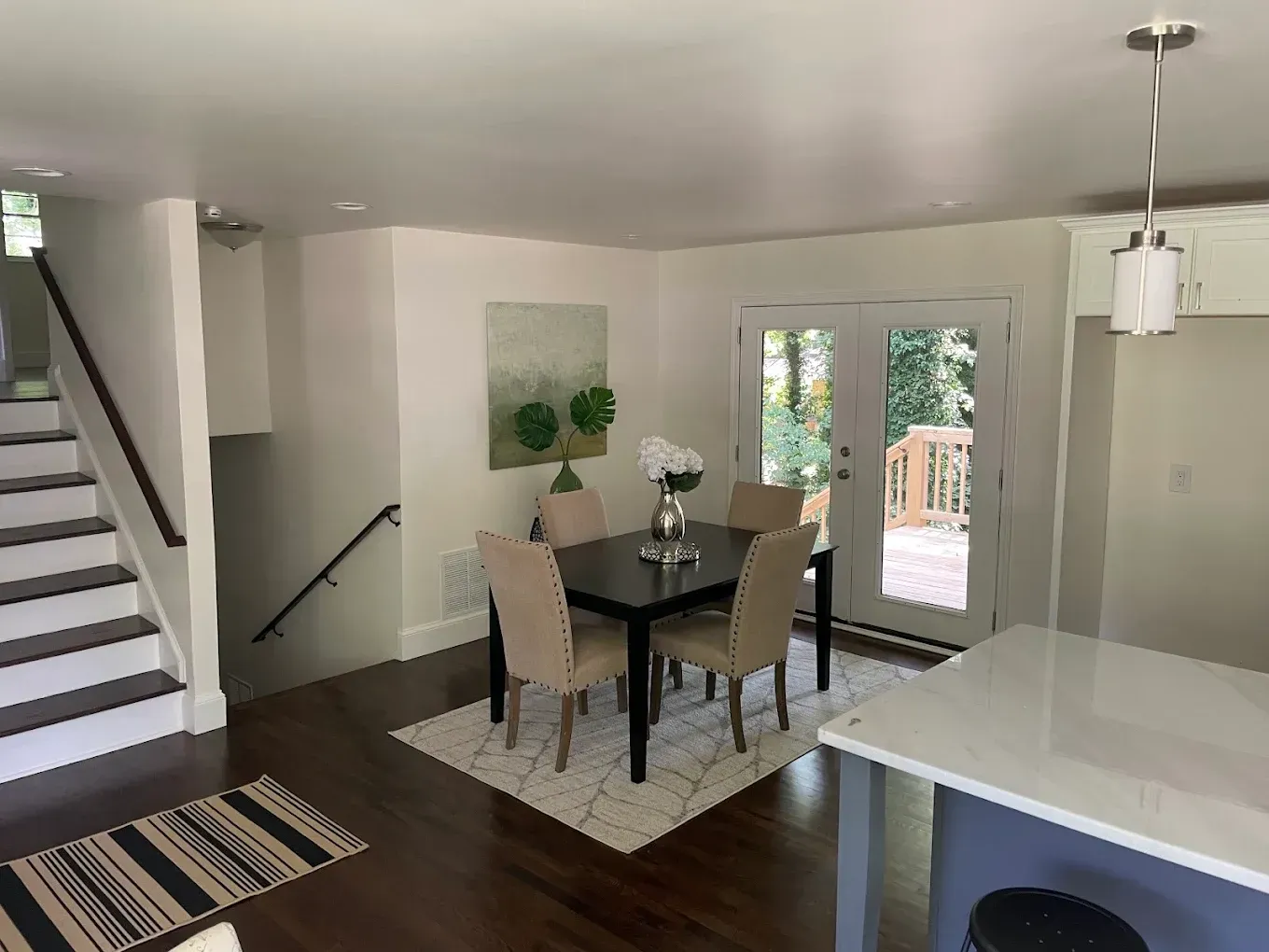 Bright dining room with dark table, beige chairs, staircase, and glass doors opening to a patio.