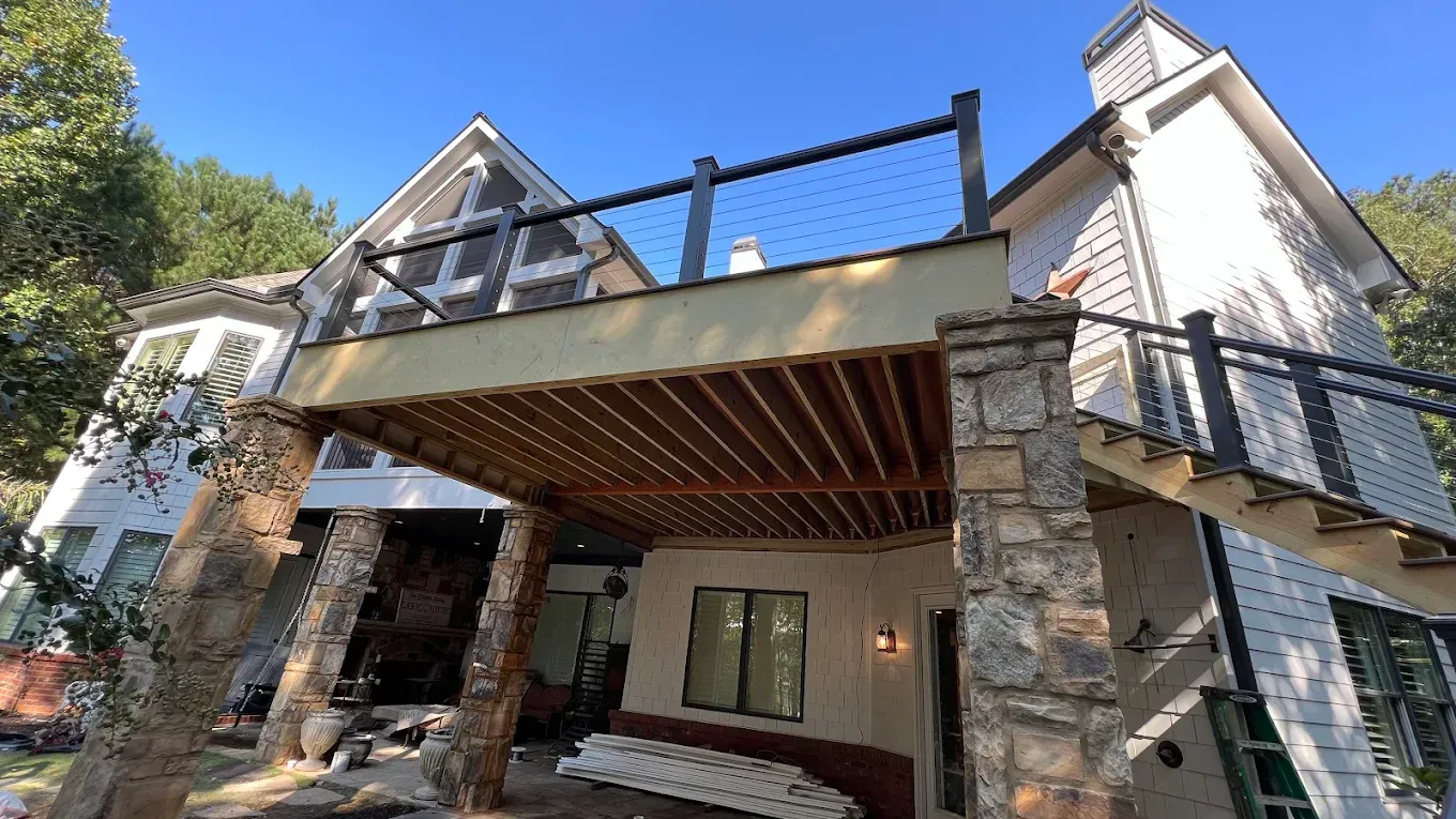 Modern house exterior with stone pillars, a wooden porch ceiling, and rooftop deck under a bright sky