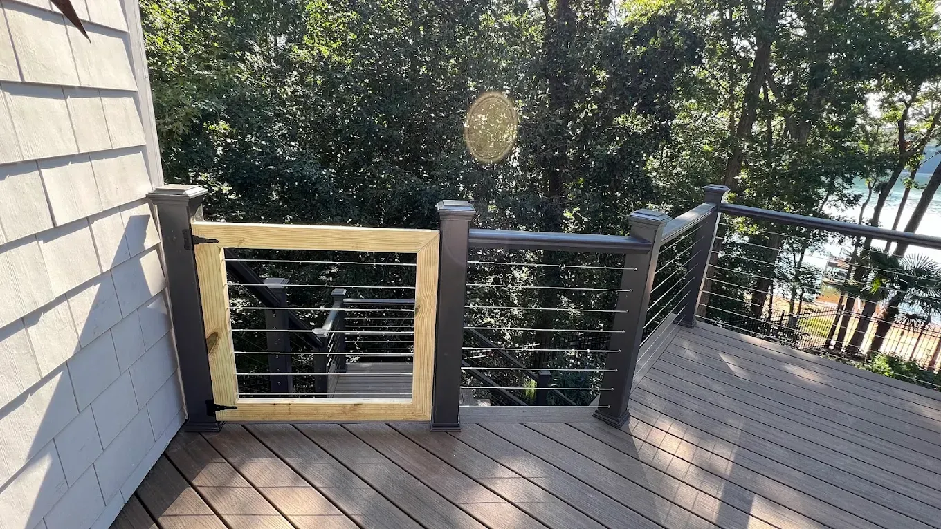 Wooden deck with railing and stairs beside a house, overlooking trees in bright sunlight