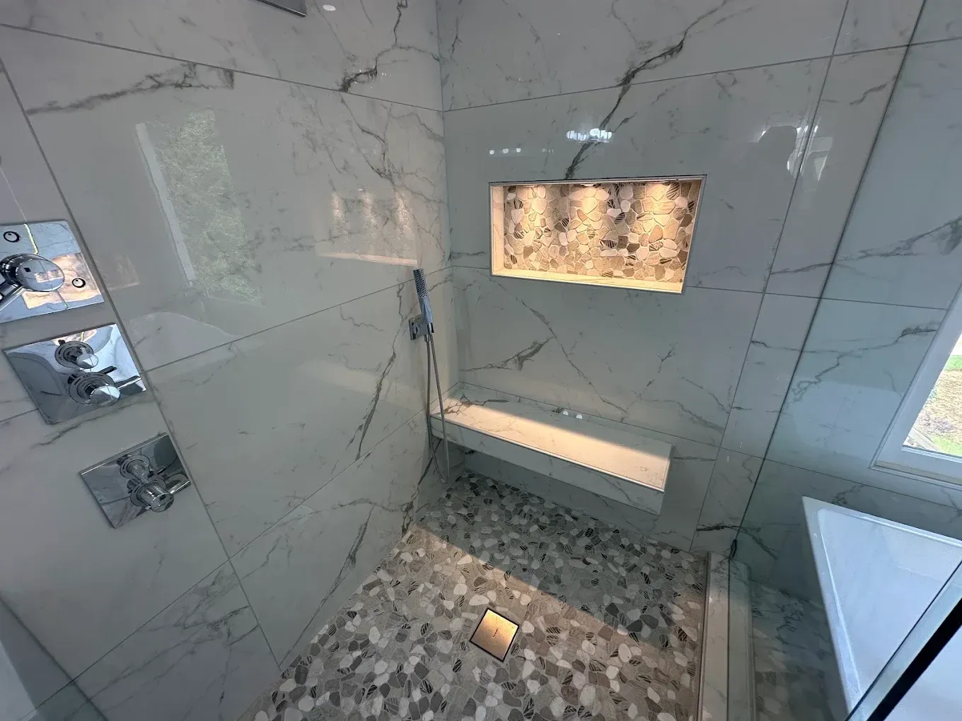 Modern bathroom with white marble walls, mosaic tile floor, and a lit recessed niche above a tub or shower.