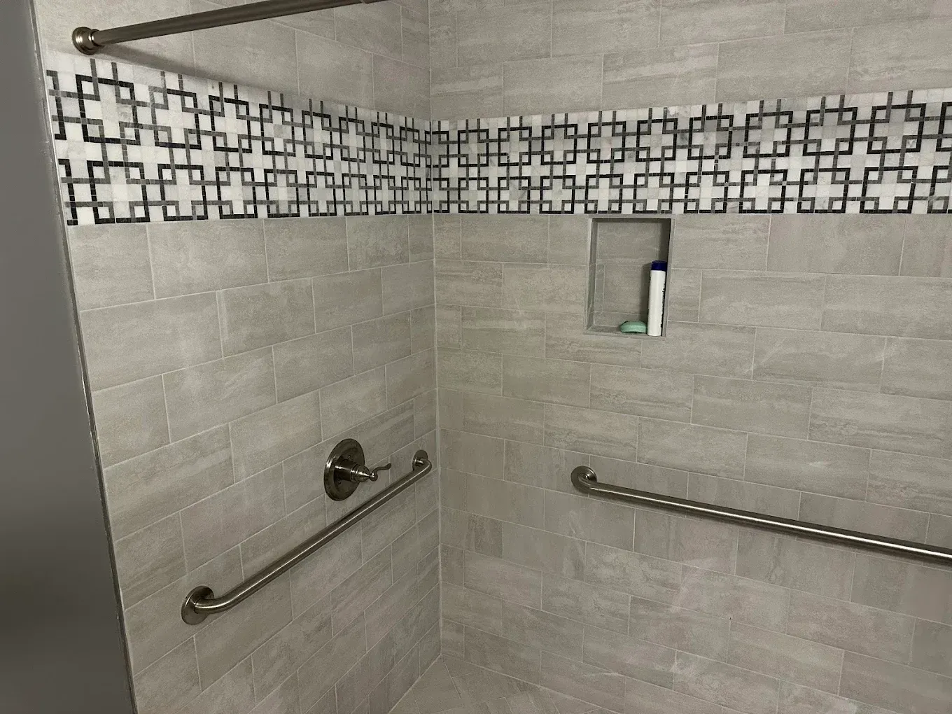 Accessible shower stall with gray tile, decorative border, and grab bars on two walls
