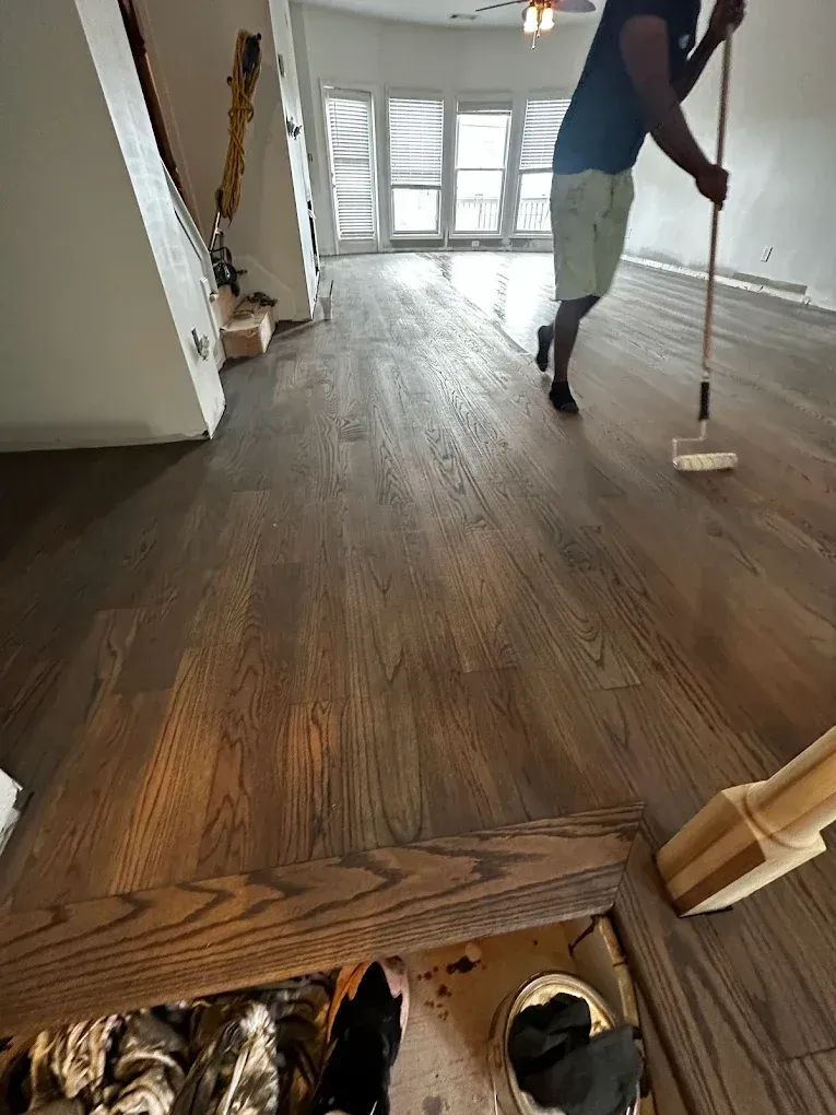 Person mopping a wood floor in a bright, empty room with large windows.