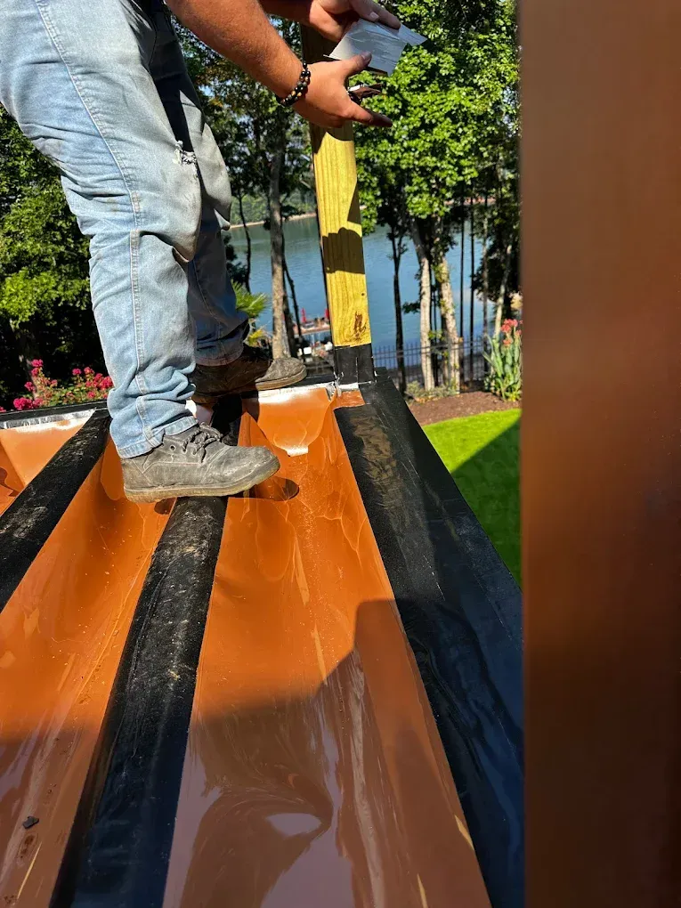 Worker applying black coating to a sloped orange surface outdoors near trees and grass