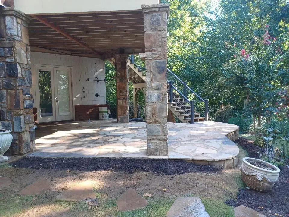 Stone patio with covered porch, stairs, and garden greenery beside a house