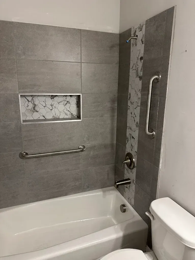 Accessible tiled bathroom with tub, grab bars, and walk-in shower controls