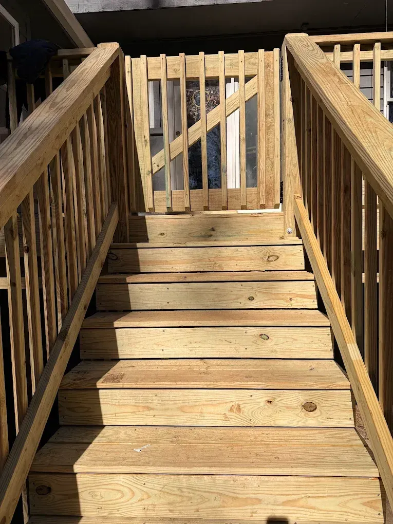 Wooden outdoor staircase with railings leading up to a gated deck under bright sunlight