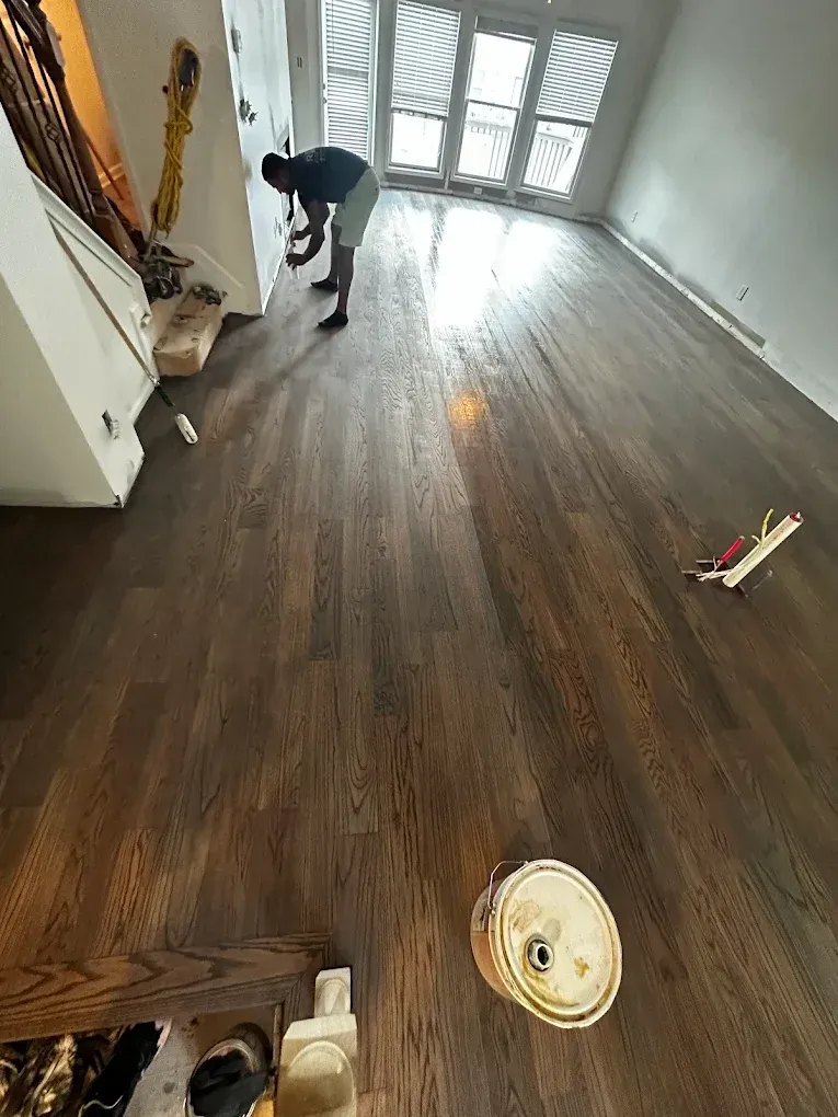 Worker installing dark wood flooring in a bright empty room