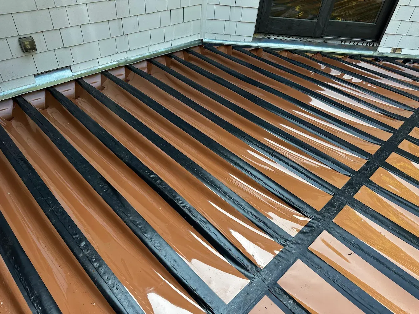 Wooden roof deck with exposed rafters and dark cross braces beside a tiled wall and window