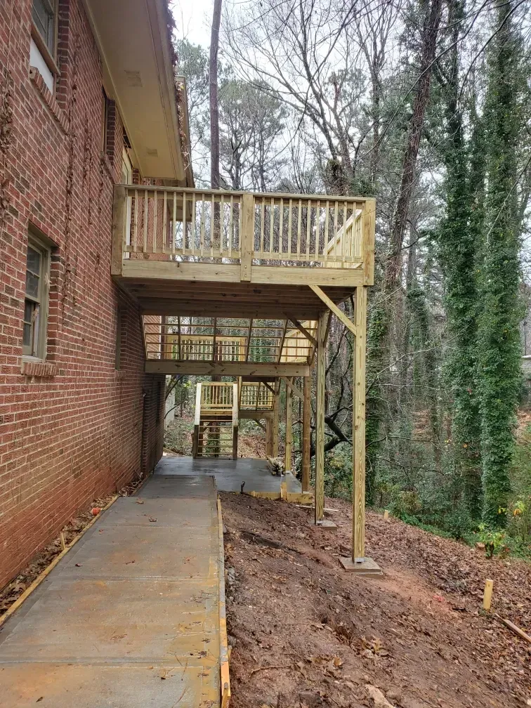 Covered wooden deck and stairs beside a brick building, overlooking a muddy wooded slope.