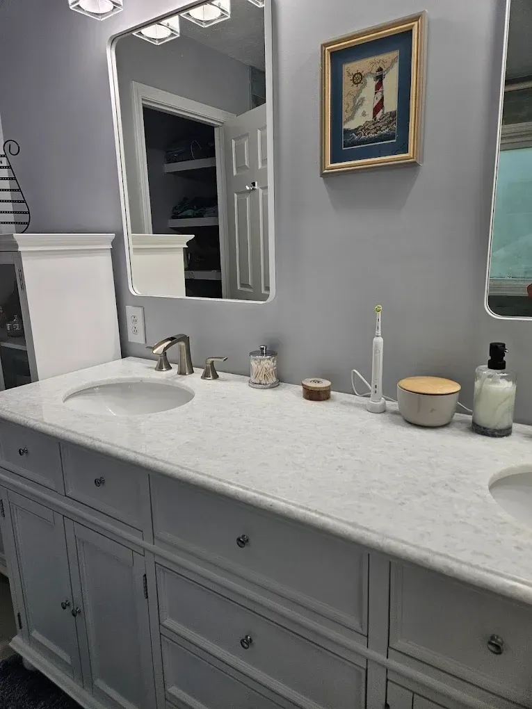 Gray bathroom vanity with white countertop, sink, mirror, and toiletries beneath framed wall art