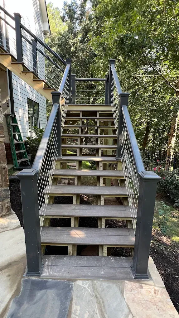 Outdoor wooden staircase with black railings leading up to a house, surrounded by trees