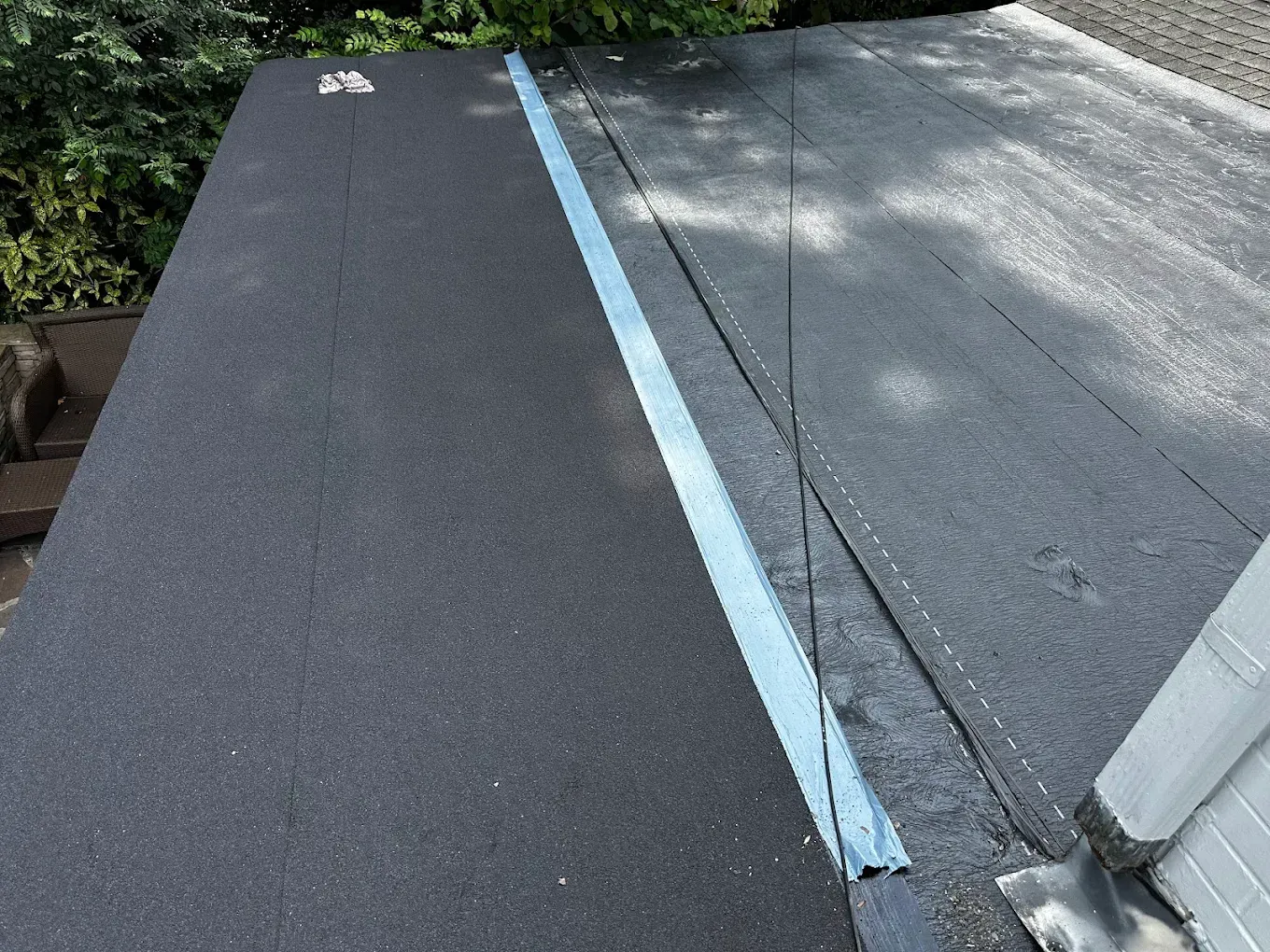Black and gray sloped roofing with a light blue seam near a wall and gutter