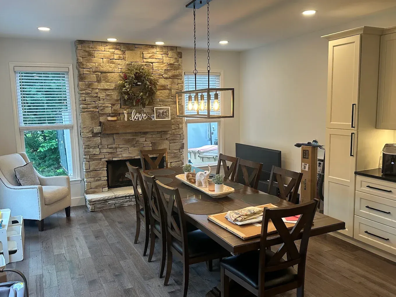 Modern dining room with stone fireplace, wooden table, dark chairs, and pendant lights