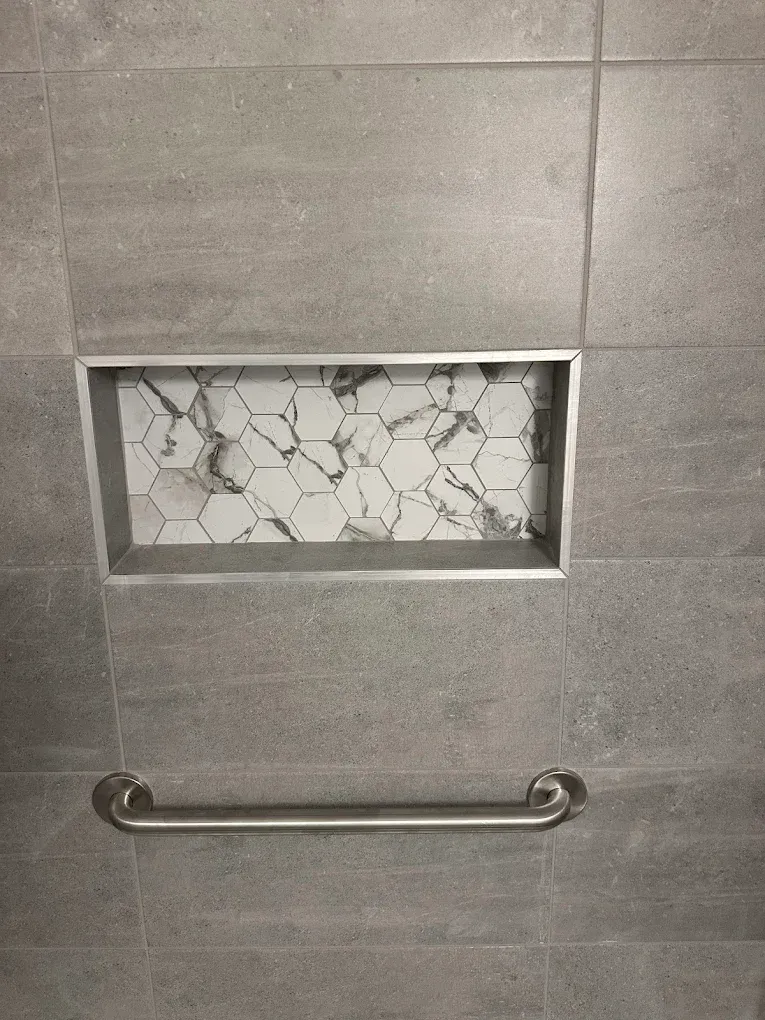 Gray tiled shower wall with recessed mosaic niche and a chrome grab bar.