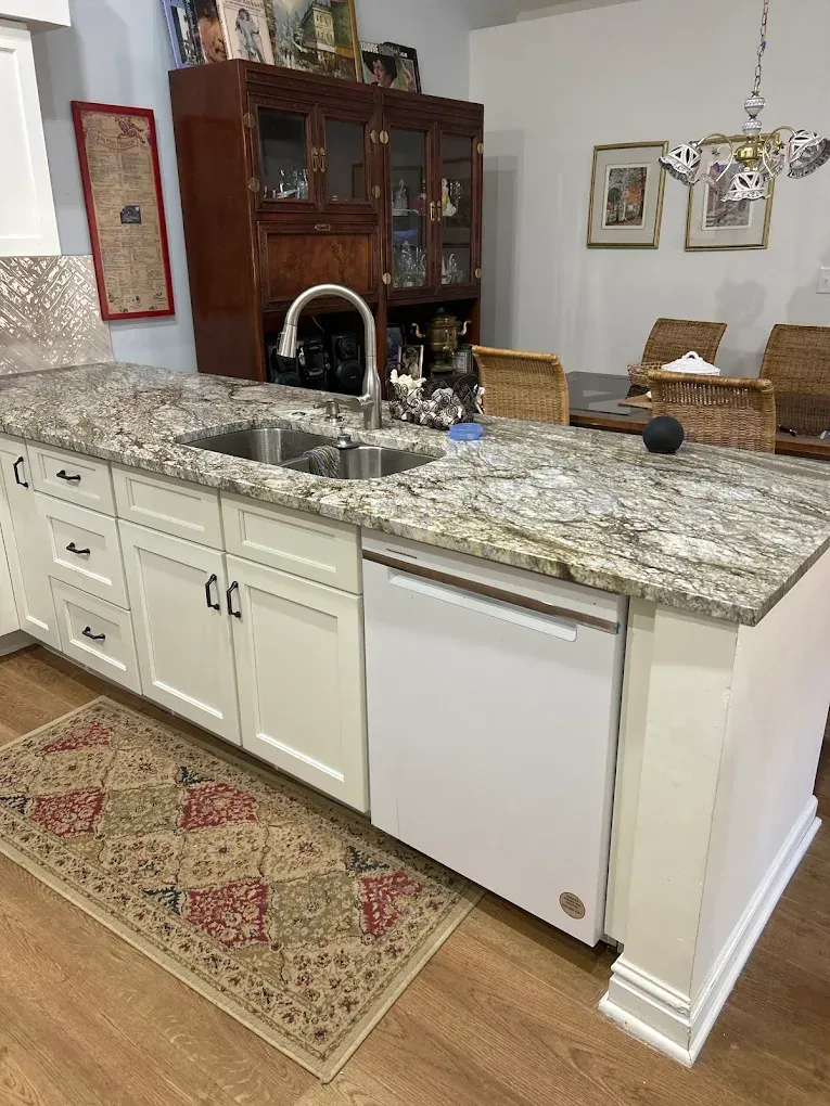 Kitchen island with granite countertop, double sink, white cabinets, and a rug on the floor