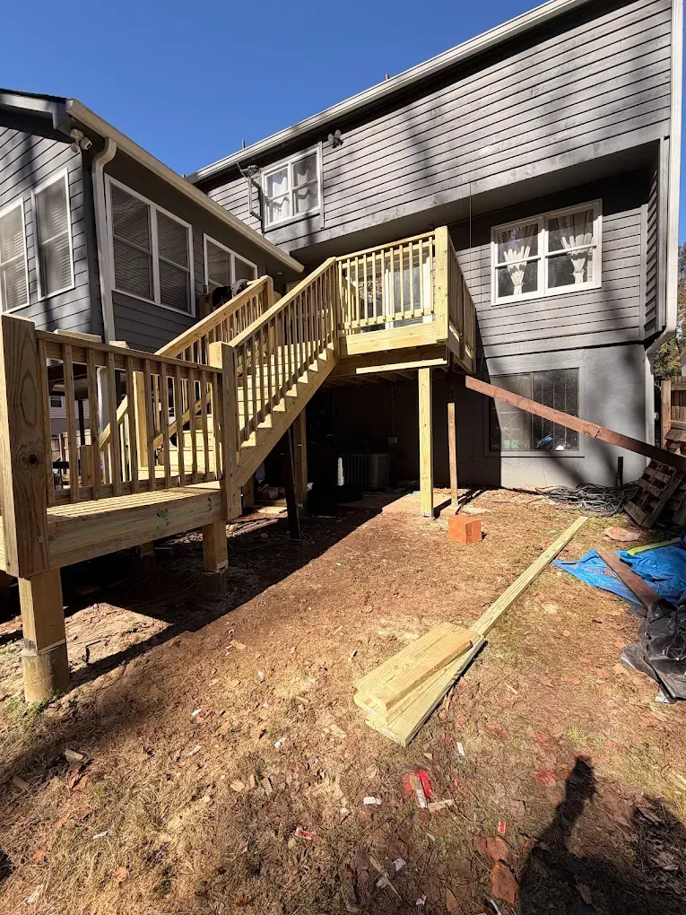 Backyard deck with wooden stairs, fenced porch, and tools scattered on bare ground below