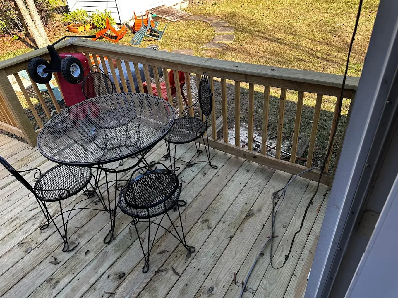 Small deck with metal table and chairs, overlooking a yard in autumn.