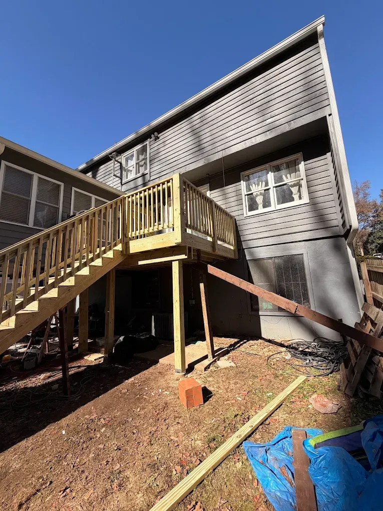 Wooden deck stairs leading to a raised gray house with siding and a sloped yard below