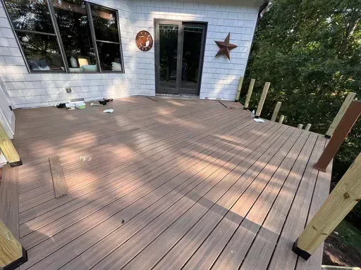Wooden deck under construction beside a house, with rail posts and a glass door.