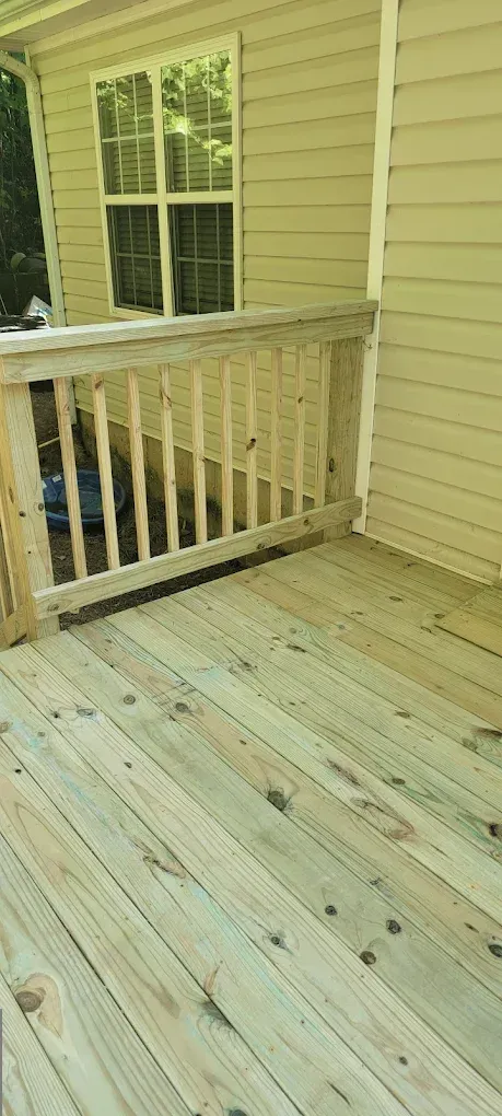 Wooden deck with white railing beside beige house siding and a window.
