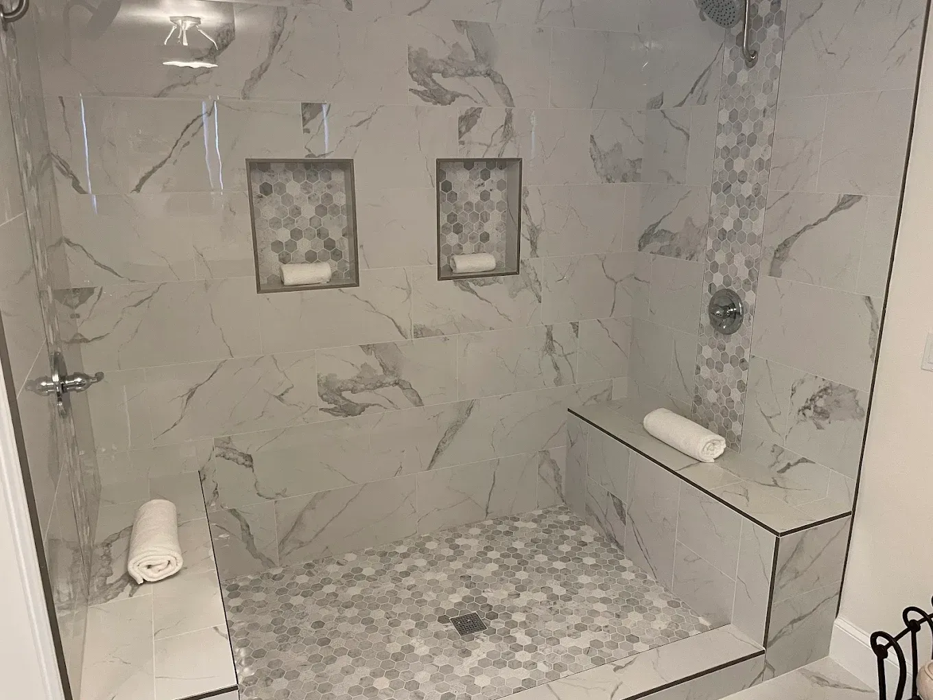 Modern tiled shower with marble walls, glass door, built-in shelf, and pebble stone floor