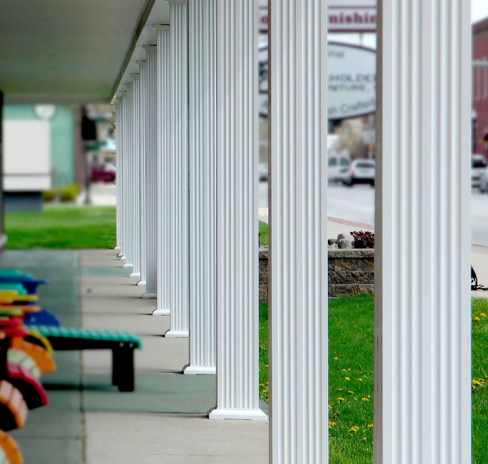 Row of white fluted columns along a building's porch, sidewalk in foreground, street in background.