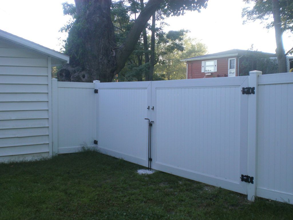 White vinyl fence with gate, set against a lawn and adjacent to a white shed.