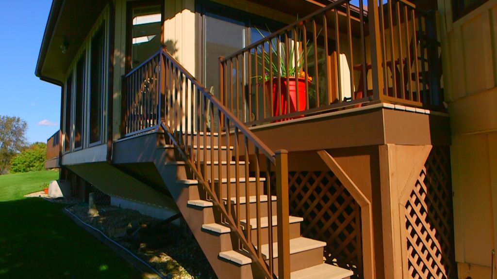 Brown wooden deck with stairs leading down to the lawn, connected to a light-colored house.