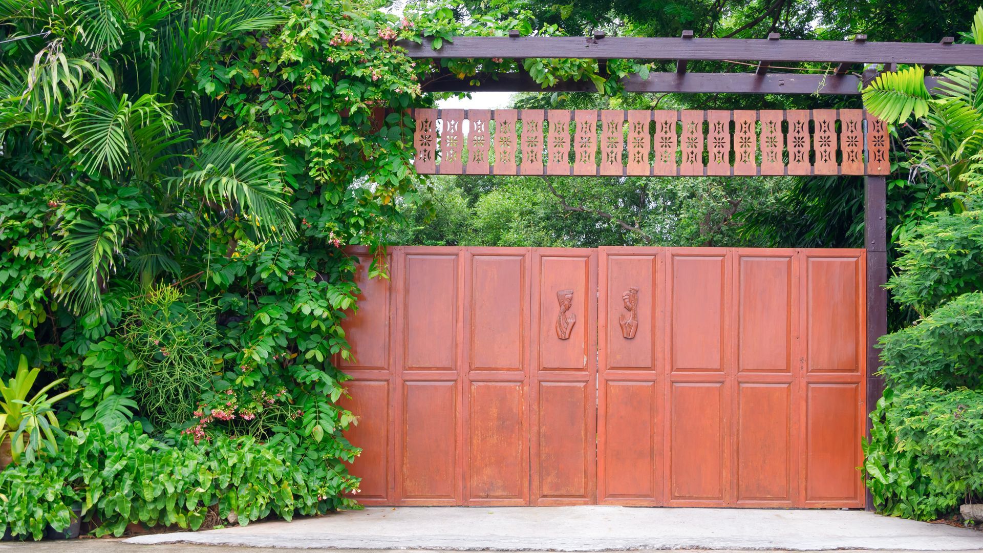 Brown gate covered with vines, leading to greenery with a wooden sign.